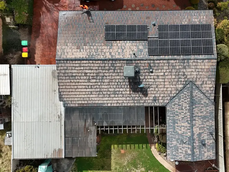 Drone view of a weathered, patchy tiled roof with solar panels, before restoration
